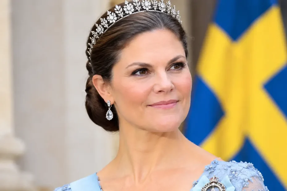 Victoria von Schweden mit funkelnder Tiara, eleganten Ohrringen und hellblauem Abendkleid vor einer schwedischen Flagge.